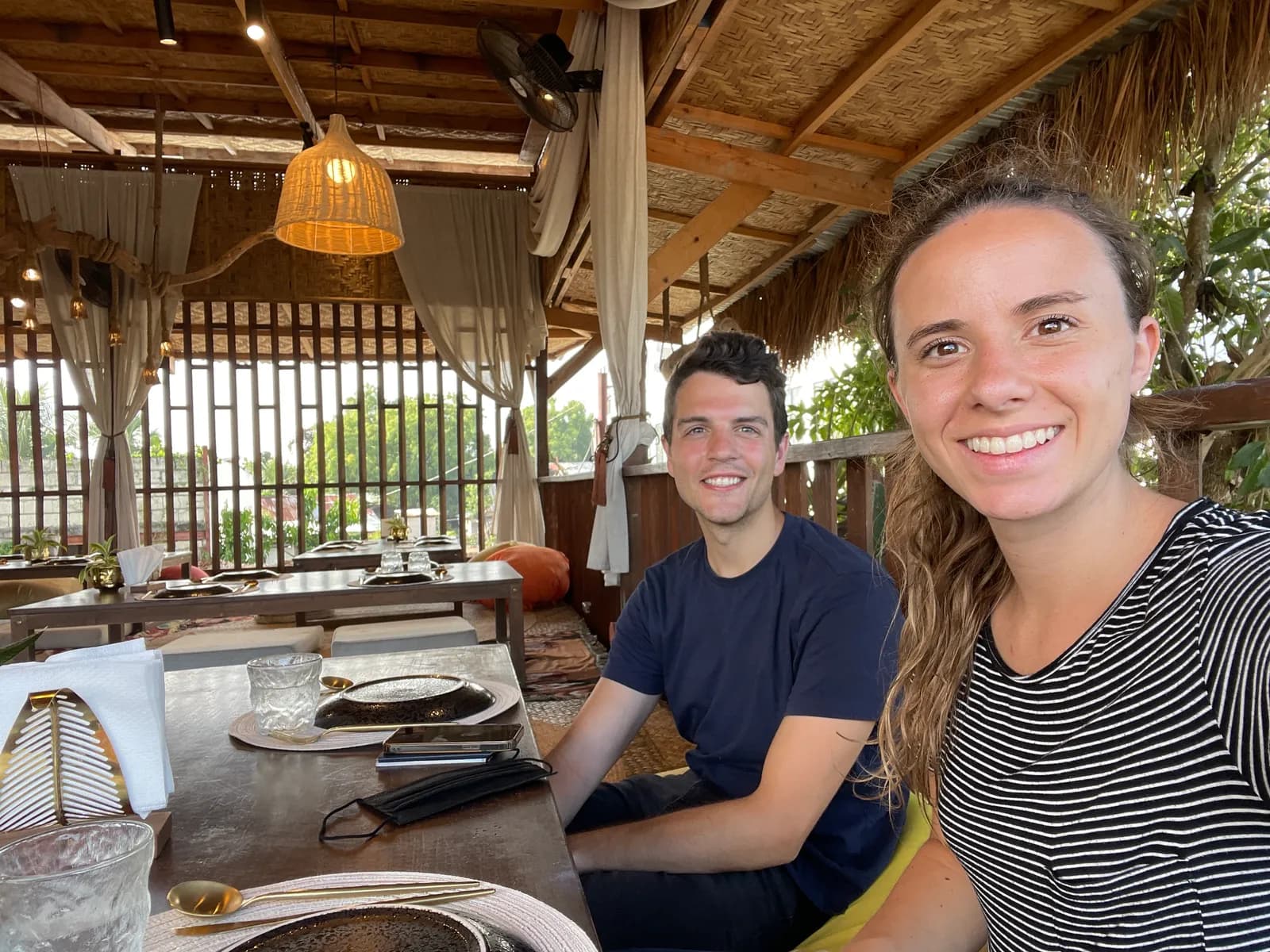 Nick and a companion at a table under a thatched roof